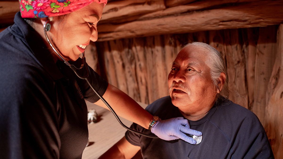 A healthcare worker listening to an older patient's heartbeat with a stethoscope